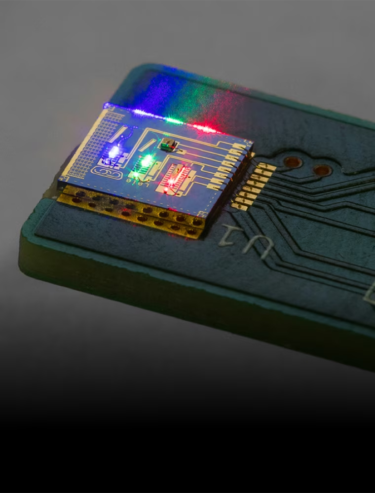 An eye-level medium shot captures a single circuit board with green, blue, and red lights illuminated on its blue component, marked "U1", "D1", "D2", and "D3", in a dark setting, under soft lighting.