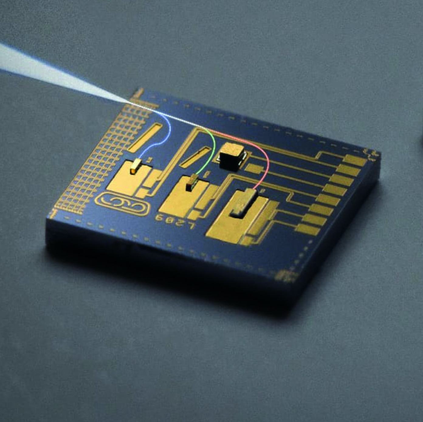 An overhead closeup shows a computer chip on a gray surface, illuminated by a white light source coming from the upper left. The chip is square-shaped with golden circuits, and a small black rectangular component sits on its right side.